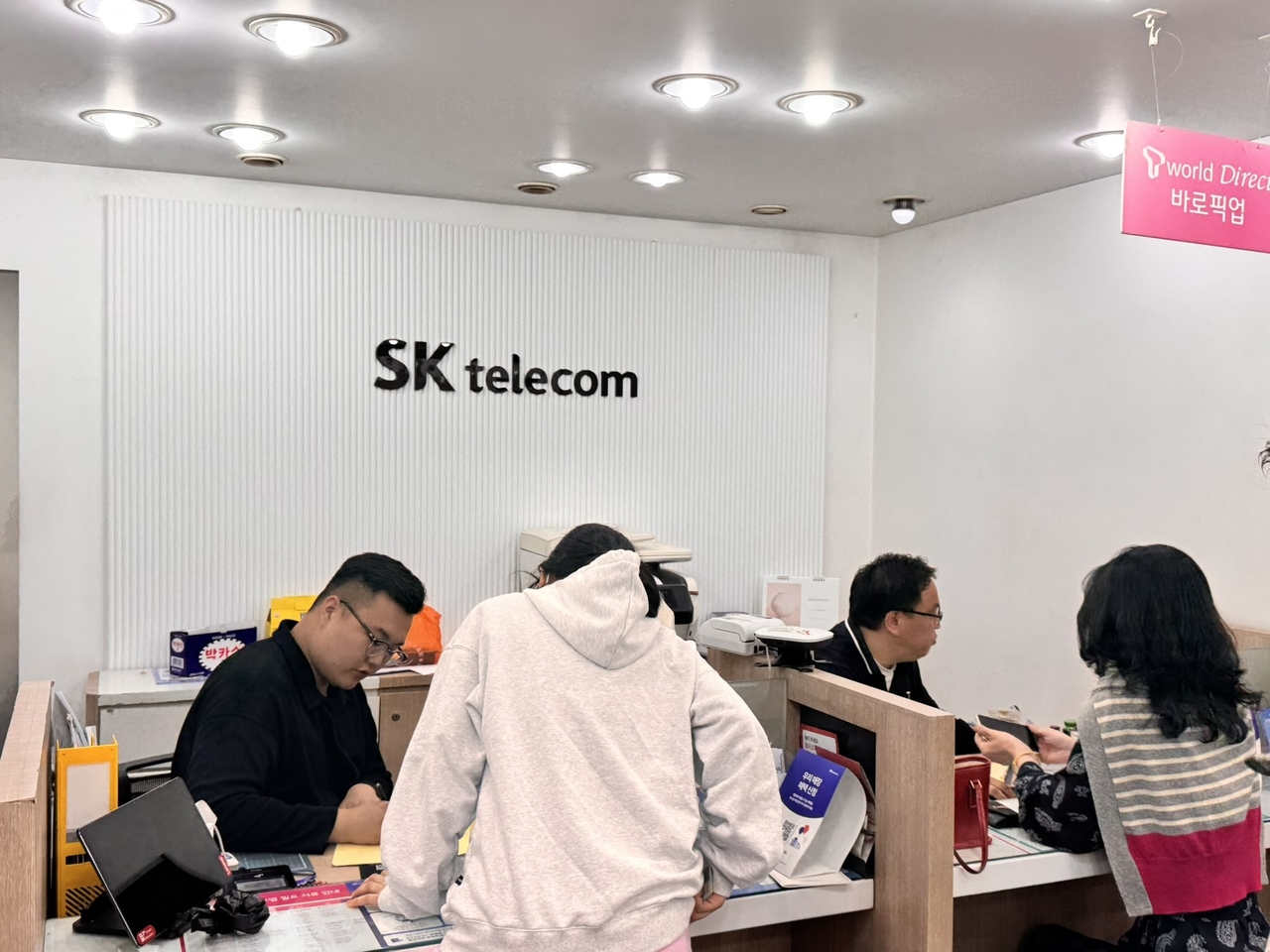 Two SK Telecom employees assist customers with new USIM card reservations at SK Telecom's branch near Sookmyung Women’s University subway station in Seoul on Monday (Moon Joon-hyun/The Korea Herald).