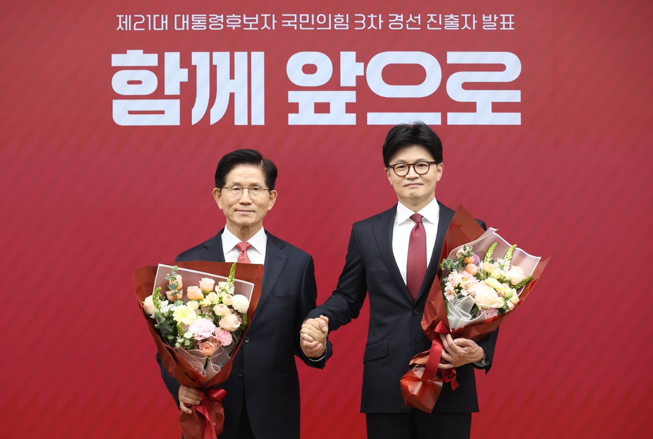 Former Labor Minister Kim Moon-soo (left) and former People Power Party Chair Han Dong-hoon hold hands as they pose for a photo after being announced as the two finalists in the ruling party's primary for the June 3 presidential election. Yonhap