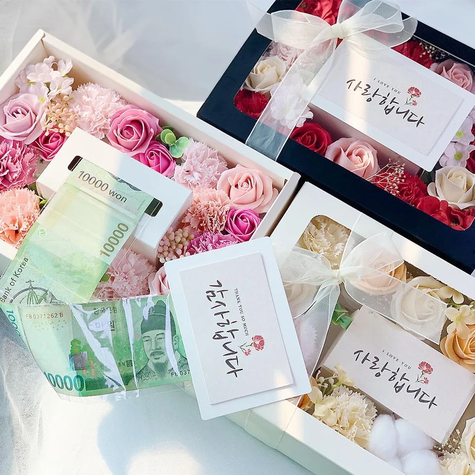 This photo shows a box full of soap flowers with a commemorative card placed in the middle for Parents' Day. When the card is pulled out, along with it comes a roll of cash. (Hello Market)