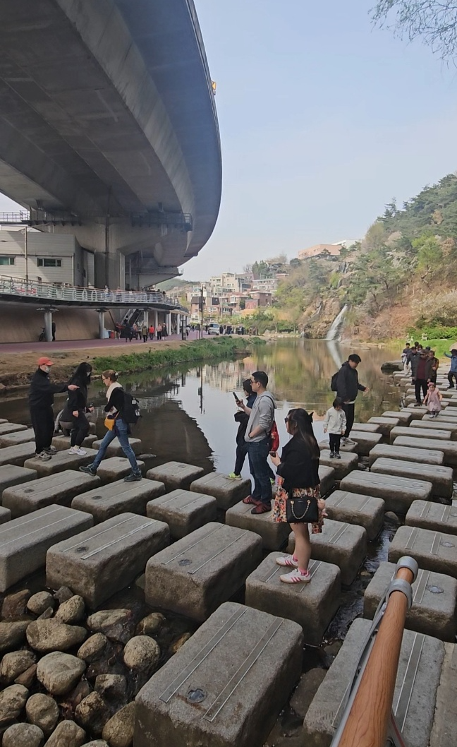 People crossing the stream on stepping stones near the artificial waterfall. (Choi Jae-hee / The Korea Herald)