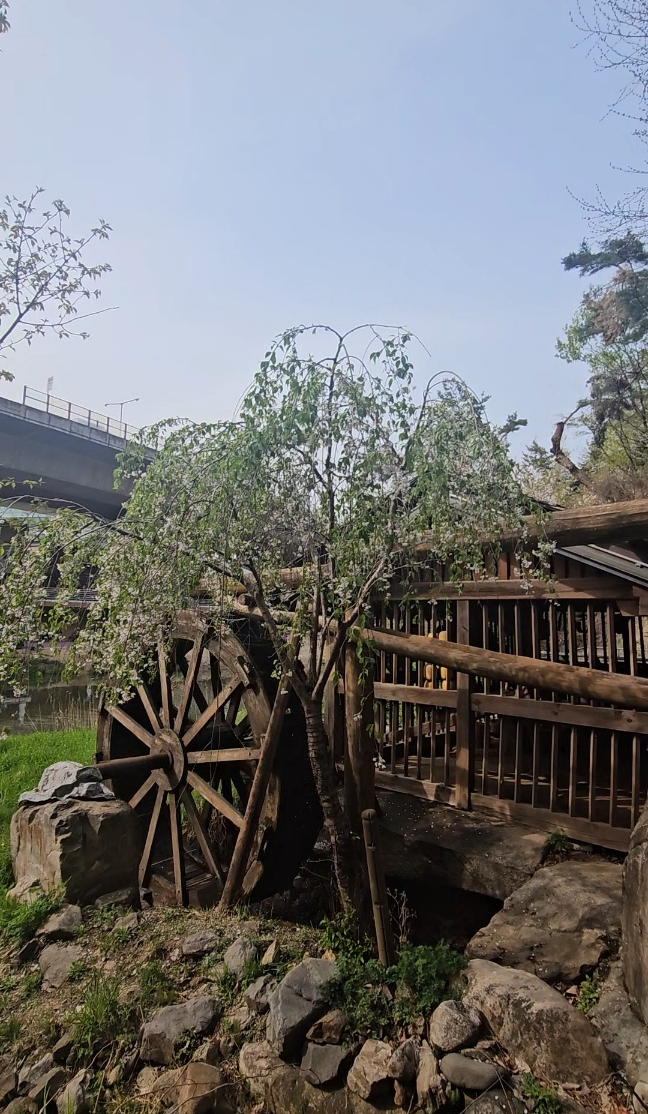 A large wooden waterwheel installed along the walking trail near the artificial waterfall. (Choi Jae-hee / The Korea Herald)